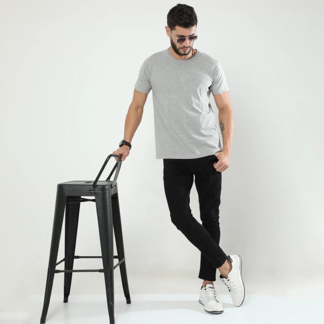 Man in gray t-shirt and black pants standing next to a black stool on a white background