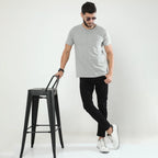Man in gray t-shirt and black pants standing next to a black stool on a white background